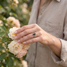 [KI] Silberring mit Onyx an der Hand zwischen Blumen