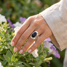 [KI] Silberring mit Onyx an der Hand zwischen Blumen