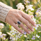 [KI] Silberring mit Onyx an der Hand zwischen Blumen
