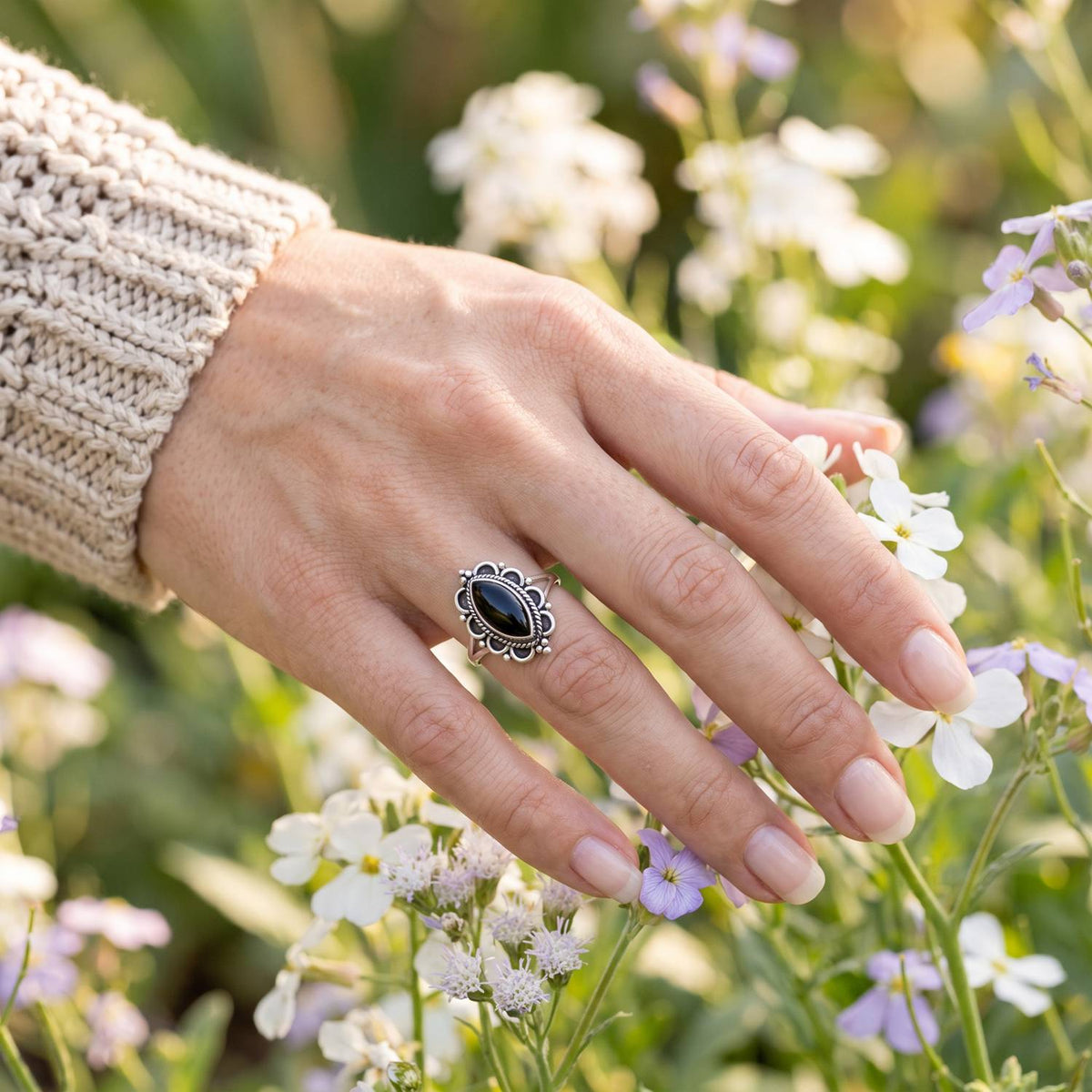 Silberring mit Onyx an der Hand zwischen Blumen