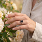 [KI] Silberring mit Onyx an der Hand zwischen Blumen
