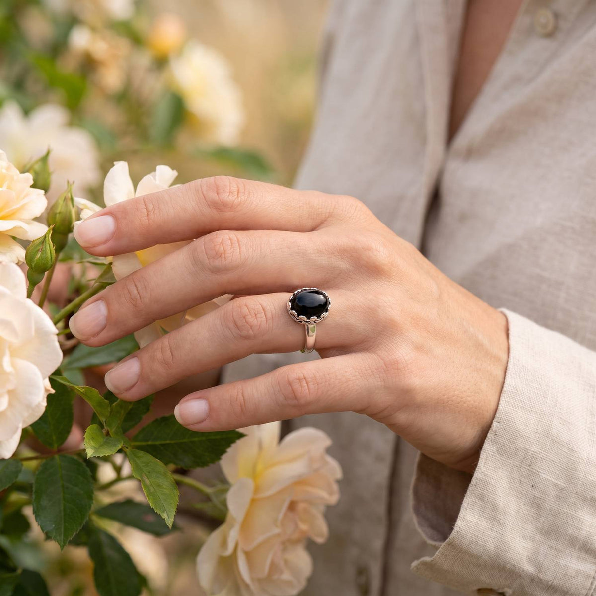 Silberring mit Onyx an der Hand zwischen Blumen