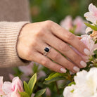 [KI] Silberring mit Onyx an der Hand zwischen Blumen