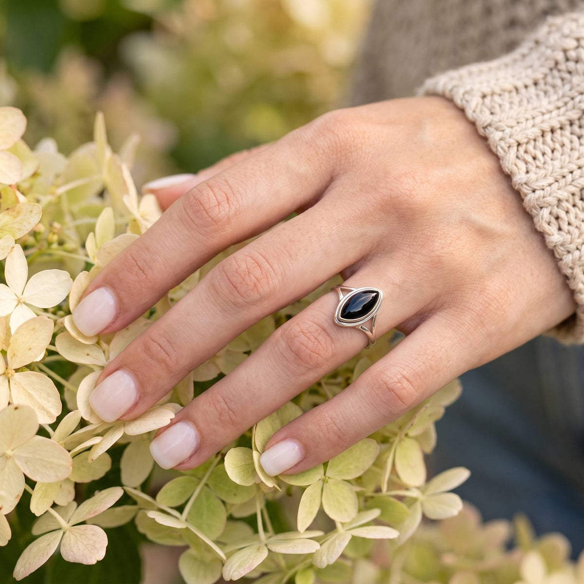 Silberring mit Onyx an der Hand zwischen Blumen