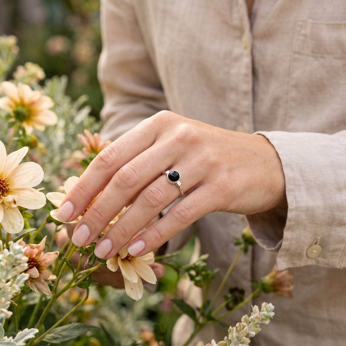 Silberring mit Onyx an der Hand zwischen Blumen