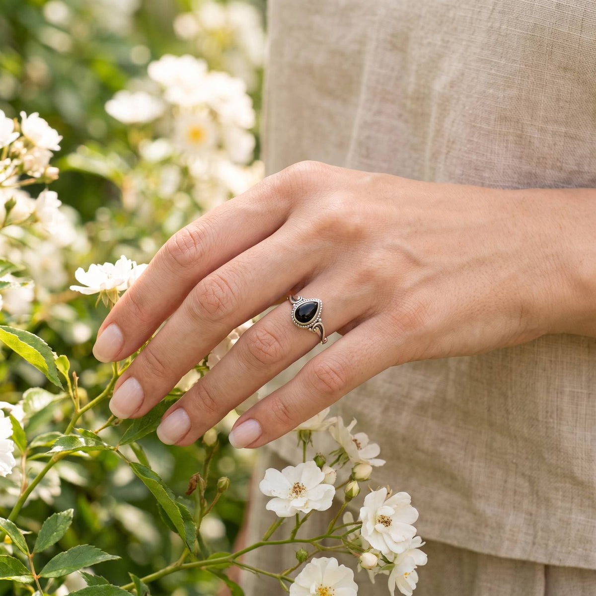 Silberring mit Onyx an der Hand zwischen Blumen
