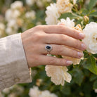 [KI] Silberring mit Onyx an der Hand zwischen Blumen