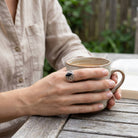 [KI] Onyxring aus Silber getragen beim Lesen mit einer Tasse