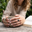 [KI] Onyxring aus Silber getragen beim Lesen mit einer Tasse