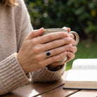 [KI] Onyxring aus Silber getragen beim Lesen mit einer Tasse