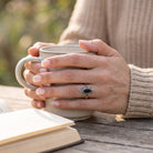 [KI] Onyxring aus Silber getragen beim Lesen mit einer Tasse