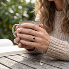 [KI] Onyxring aus Silber getragen beim Lesen mit einer Tasse