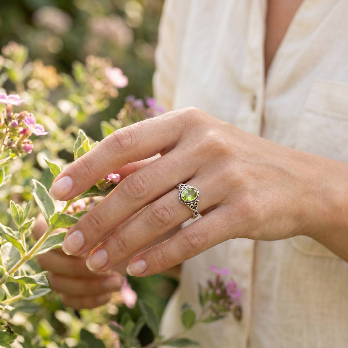 Silberring mit Peridot an der Hand zwischen Blumen