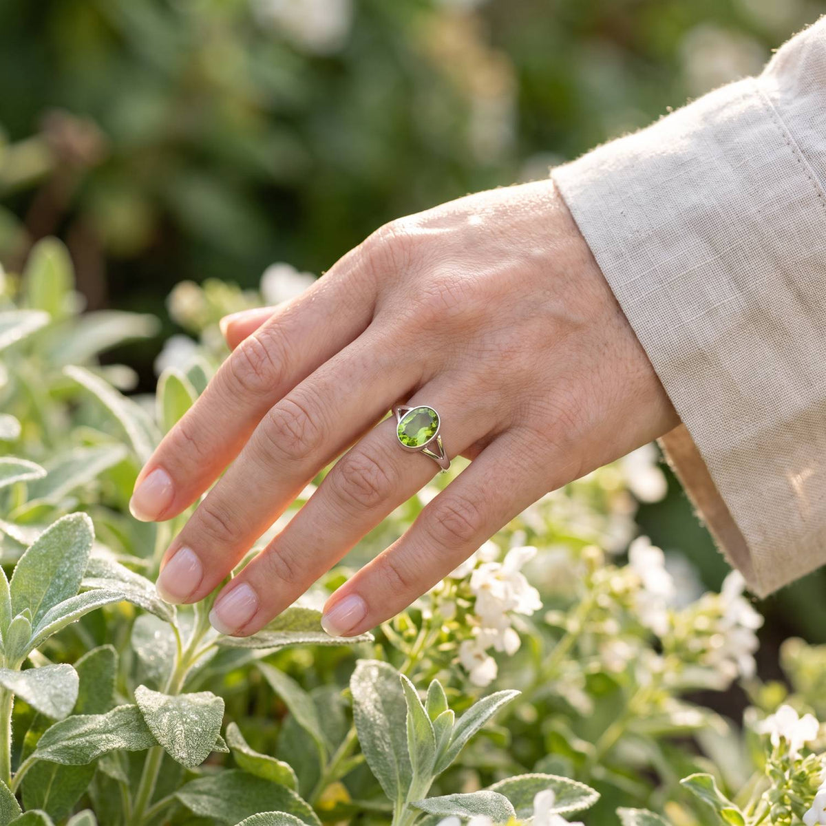 Silberring mit Peridot an der Hand zwischen Blumen