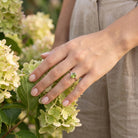 [KI] Silberring mit Peridot an der Hand zwischen Blumen
