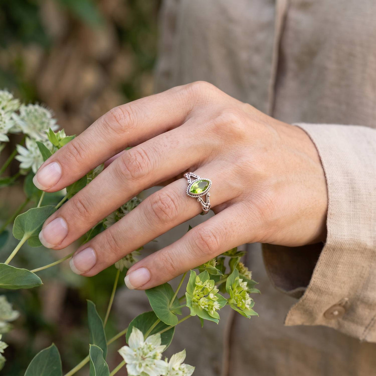 Silberring mit Peridot an der Hand zwischen Blumen