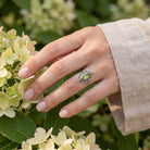 [KI] Silberring mit Peridot an der Hand zwischen Blumen