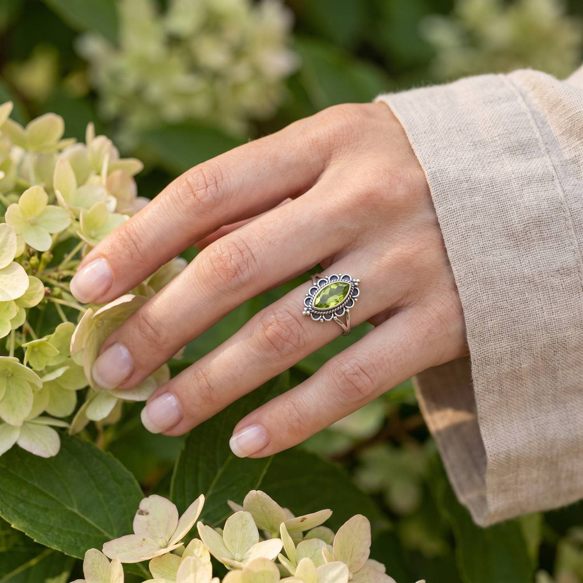 Silberring mit Peridot an der Hand zwischen Blumen