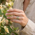 [KI] Silberring mit Peridot an der Hand zwischen Blumen