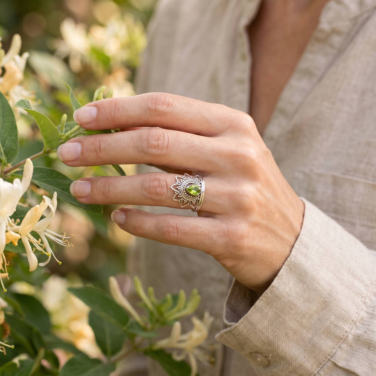 Silberring mit Peridot an der Hand zwischen Blumen