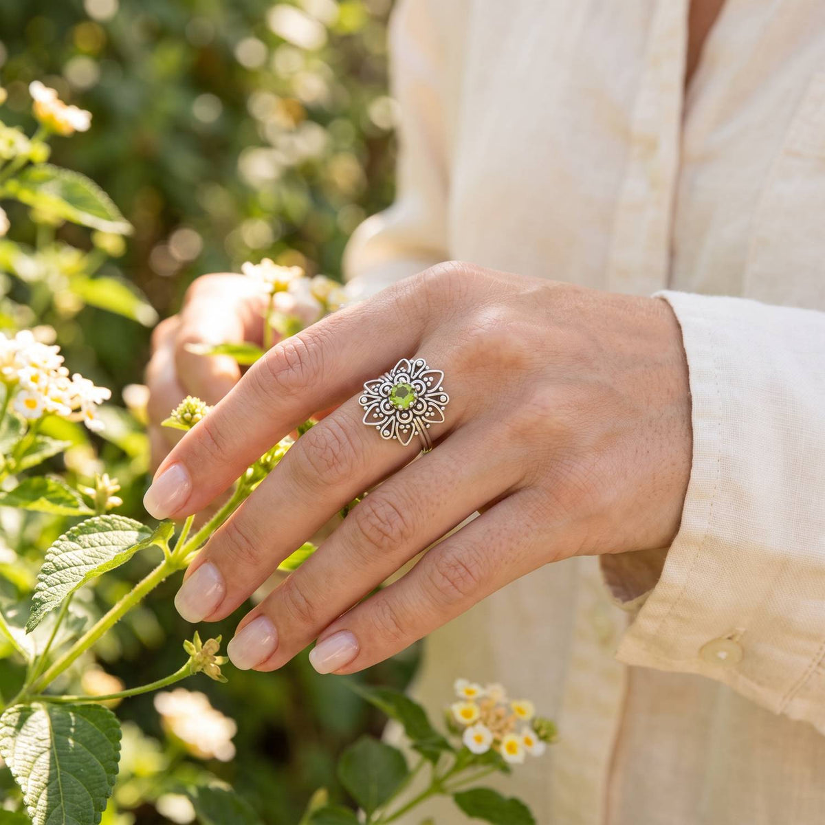 Silberring mit Peridot an der Hand zwischen Blumen