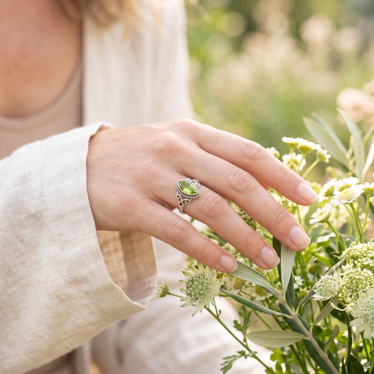 Silberring mit Peridot an der Hand zwischen Blumen
