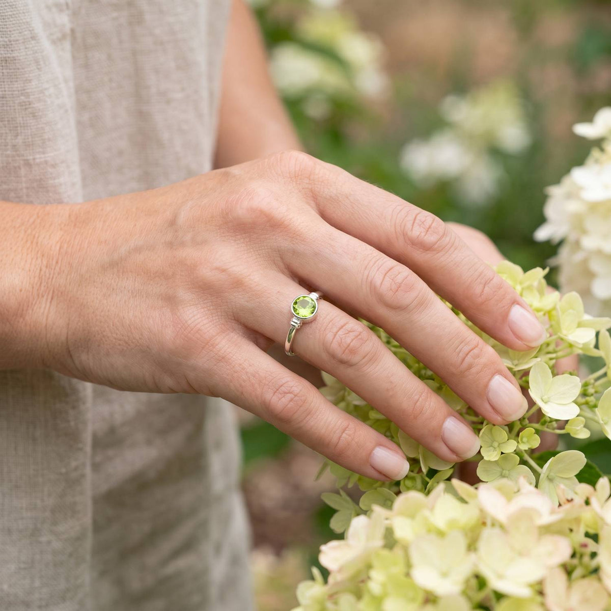 Silberring mit Peridot an der Hand zwischen Blumen