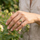 [KI] Silberring mit Peridot an der Hand zwischen Blumen