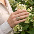 [KI] Silberring mit Peridot an der Hand zwischen Blumen
