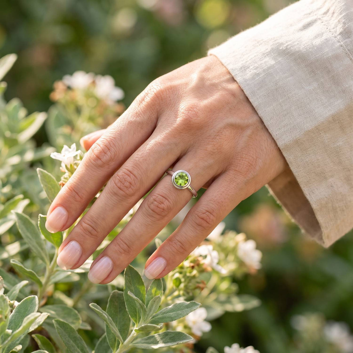 Silberring mit Peridot an der Hand zwischen Blumen