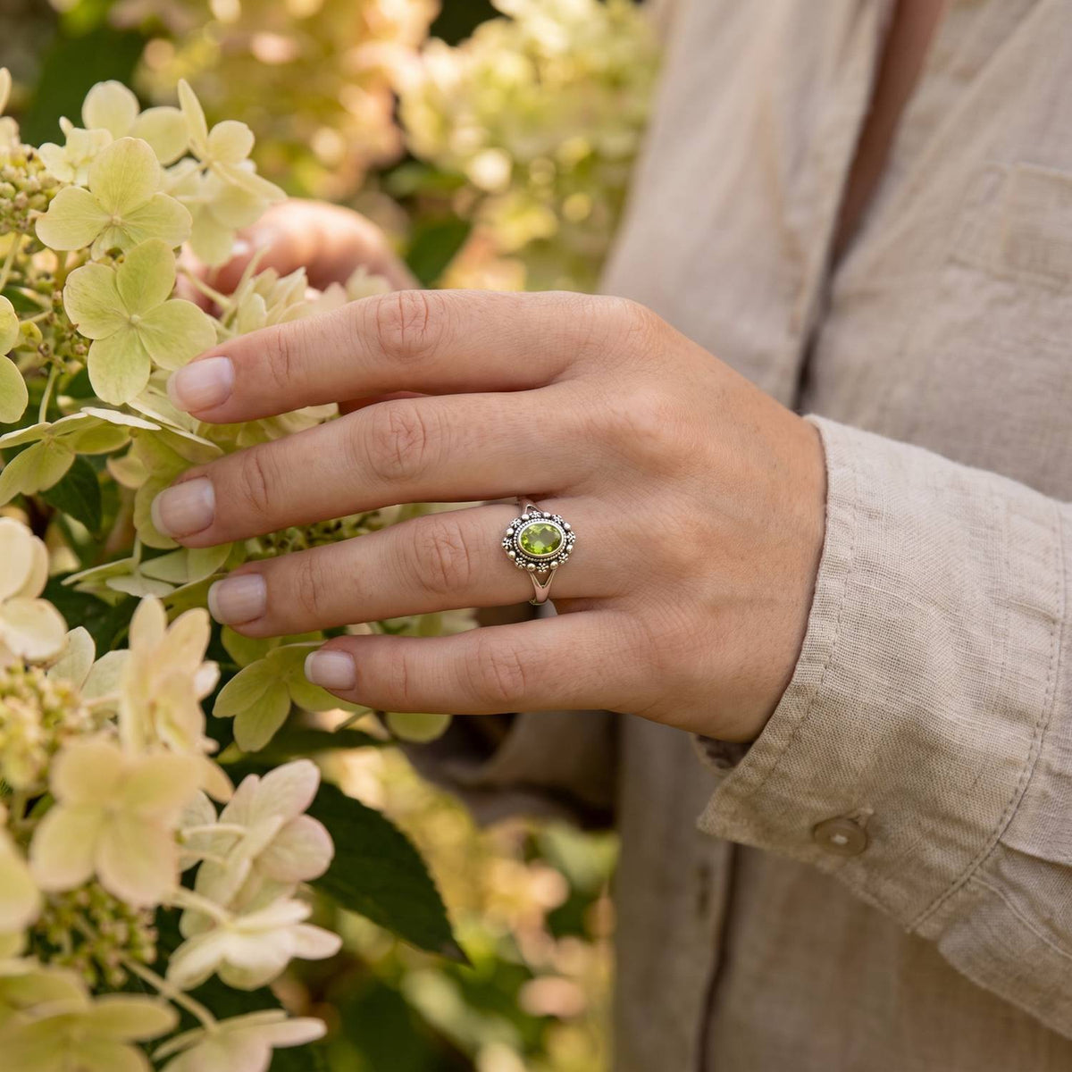 Silberring mit Peridot an der Hand zwischen Blumen