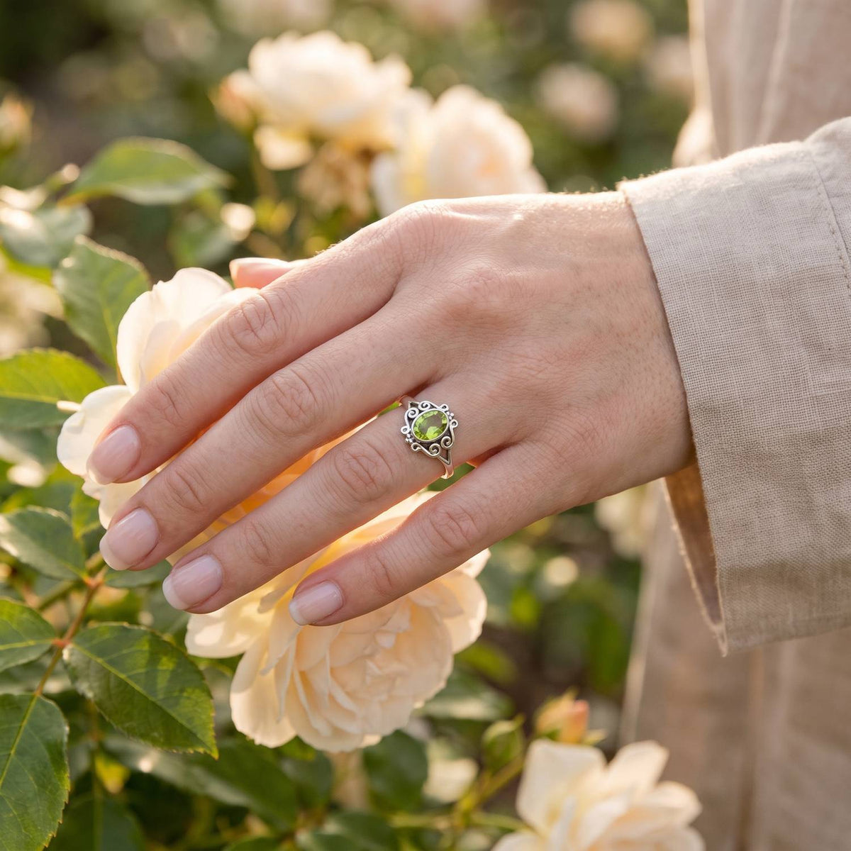 Silberring mit Peridot an der Hand zwischen Blumen