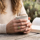 [KI] Peridotring aus Silber getragen beim Lesen mit einer Tasse