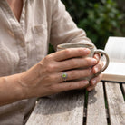 [KI] Peridotring aus Silber getragen beim Lesen mit einer Tasse