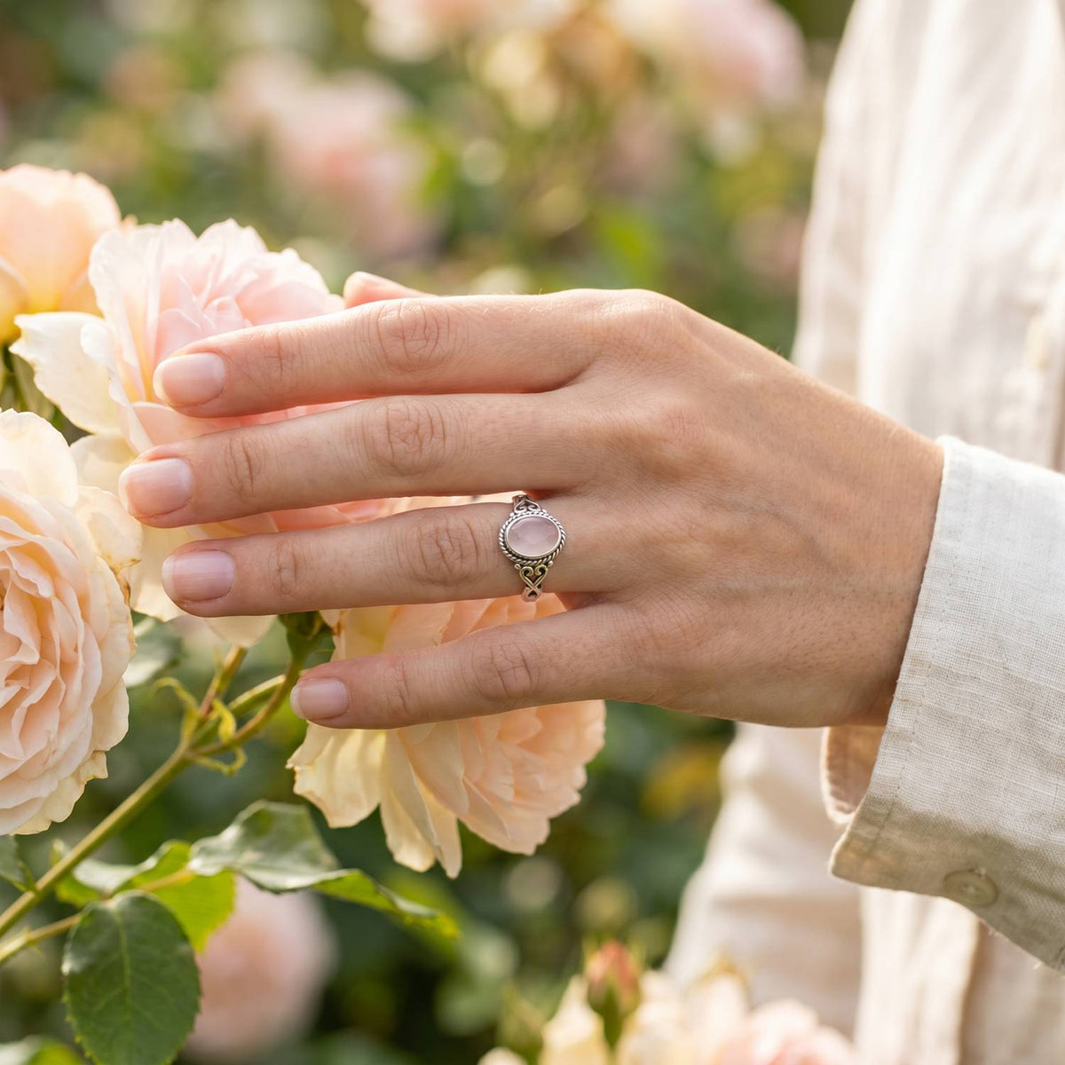 Silberring mit Rosenquarz an der Hand zwischen Blumen