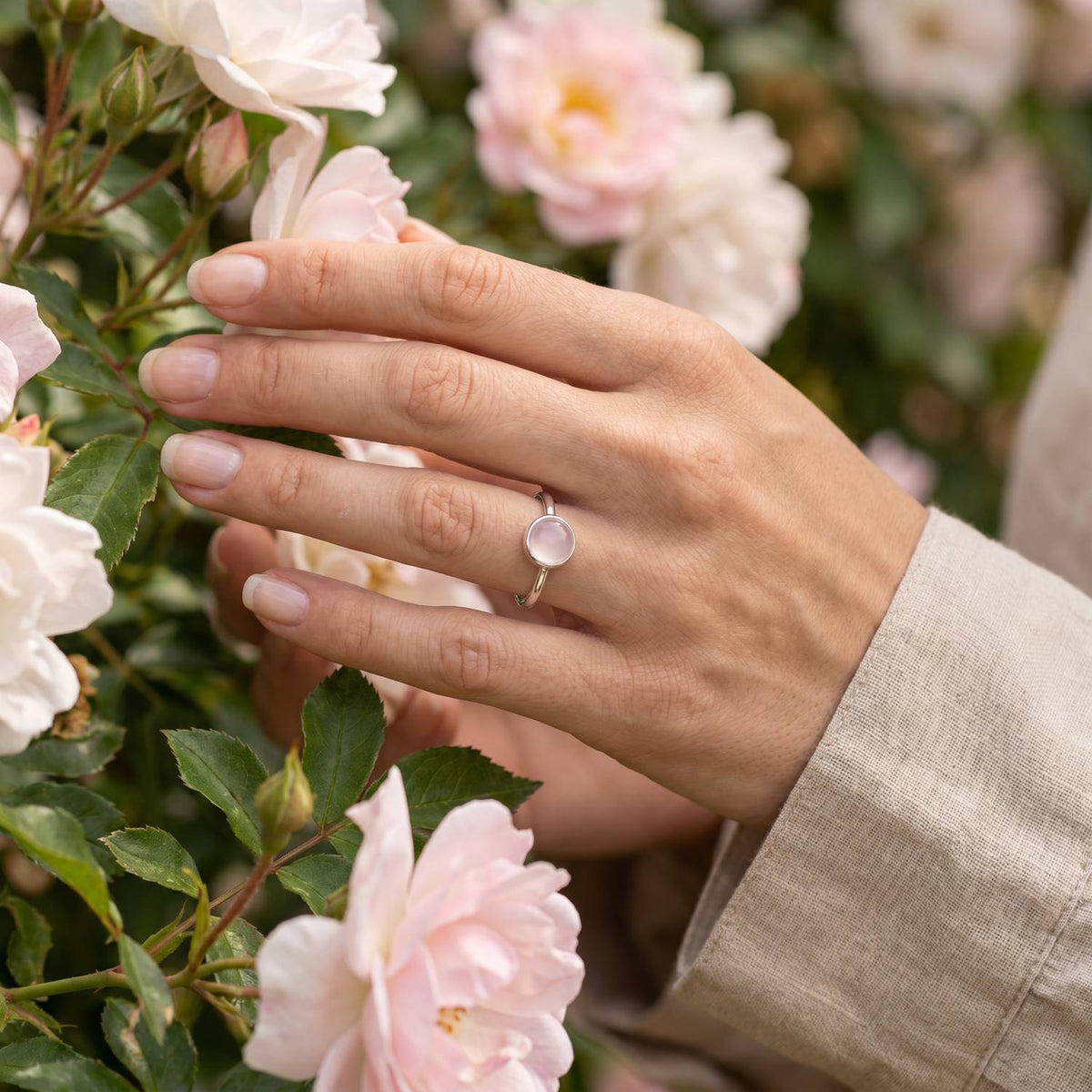 Silberring mit Rosenquarz an der Hand zwischen Blumen