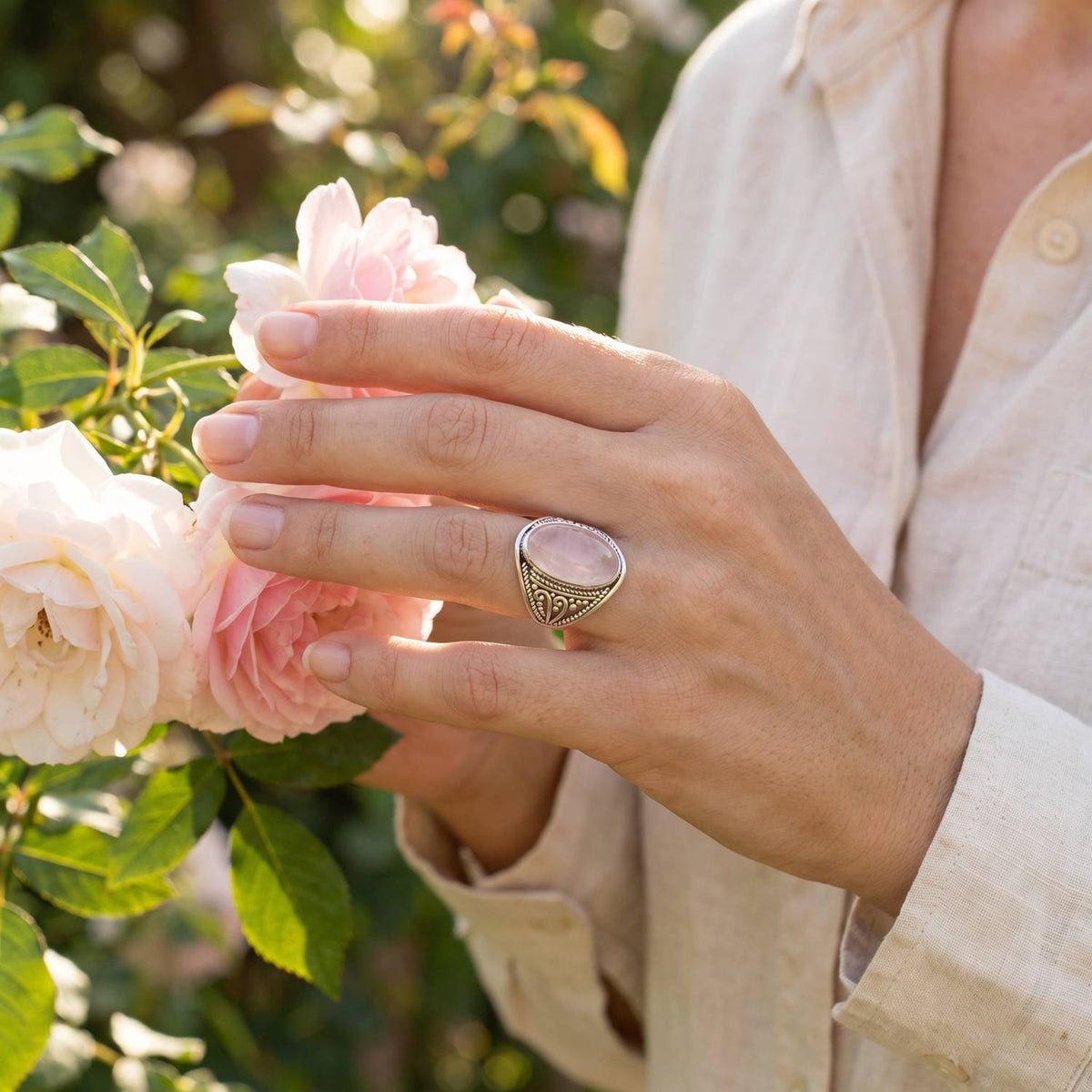 Silberring mit Rosenquarz an der Hand zwischen Blumen