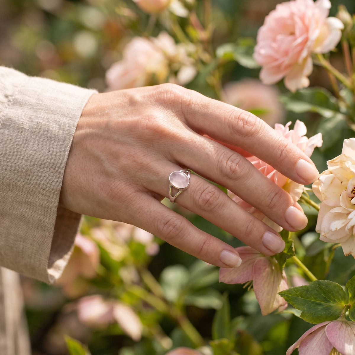 Silberring mit Rosenquarz an der Hand zwischen Blumen
