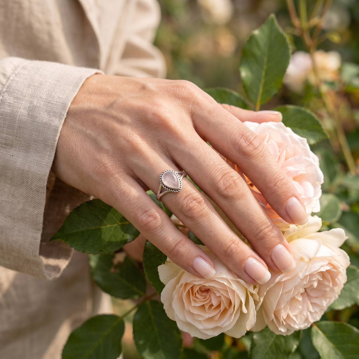 Silberring mit Rosenquarz an der Hand zwischen Blumen