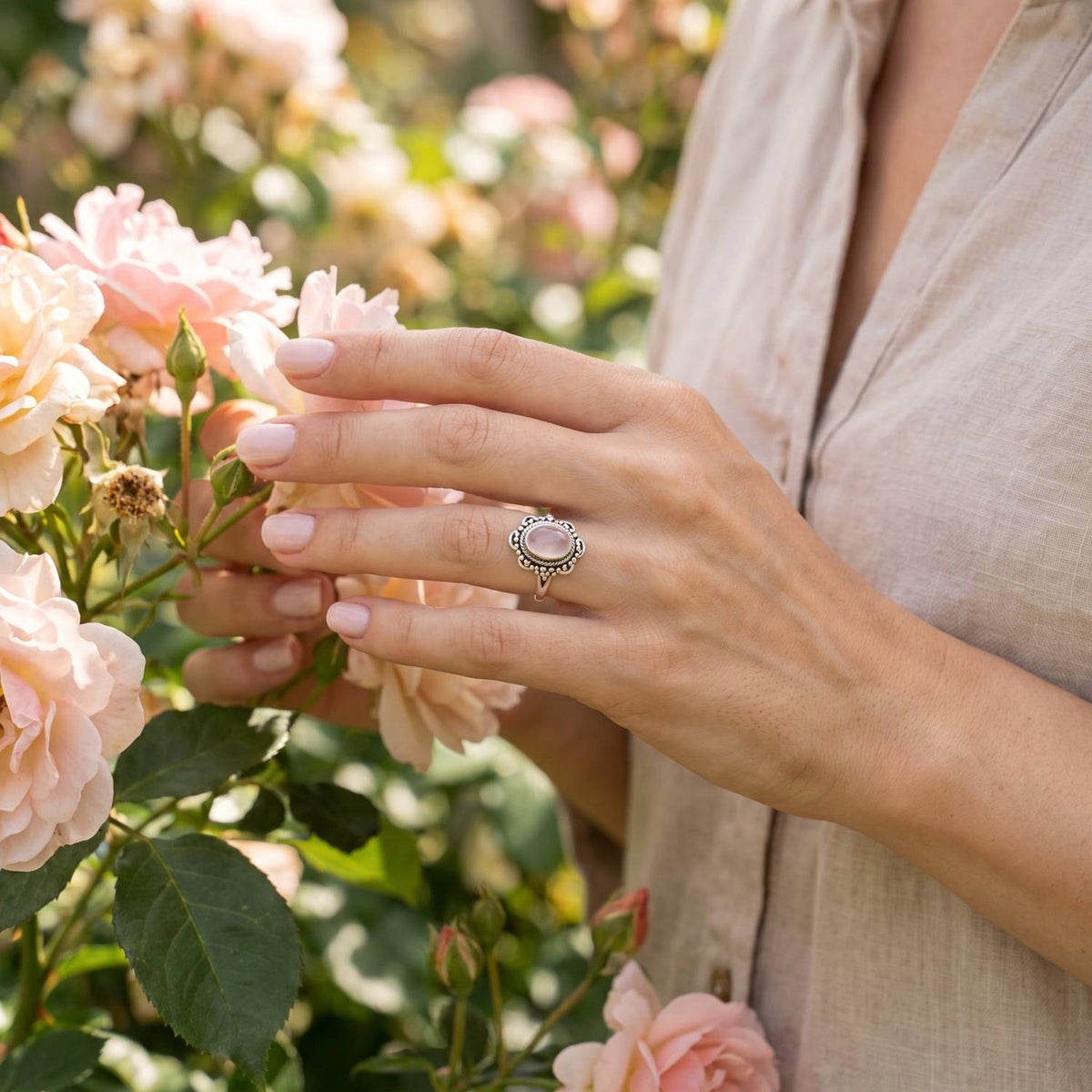 Silberring mit Rosenquarz an der Hand zwischen Blumen
