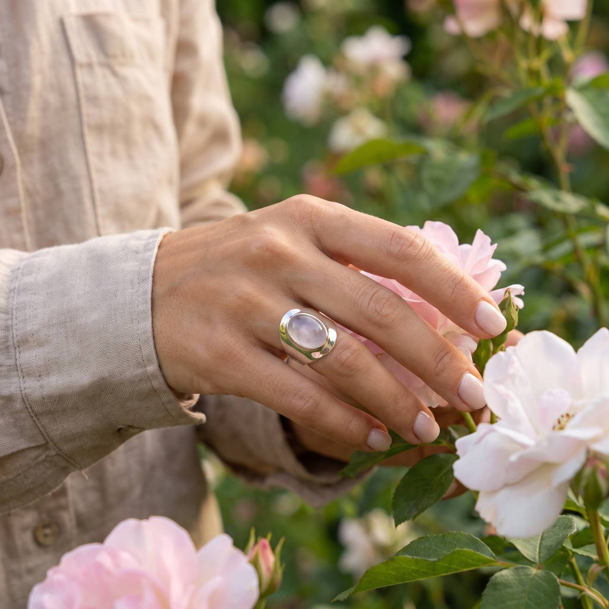 Silberring mit Rosenquarz an der Hand zwischen Blumen