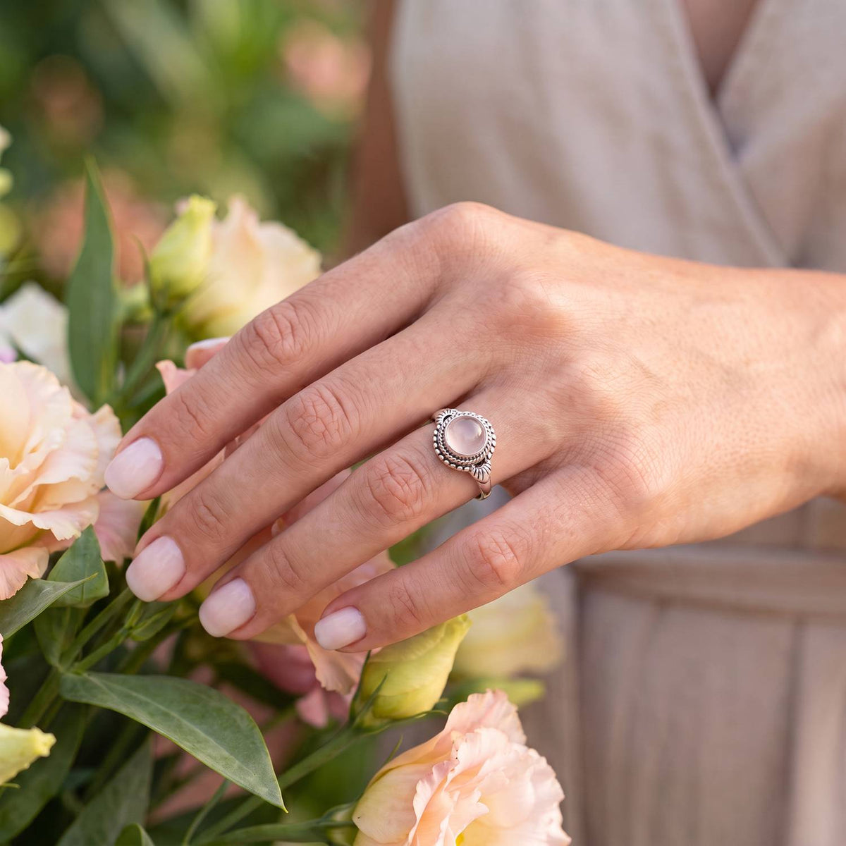 Silberring mit Rosenquarz an der Hand zwischen Blumen