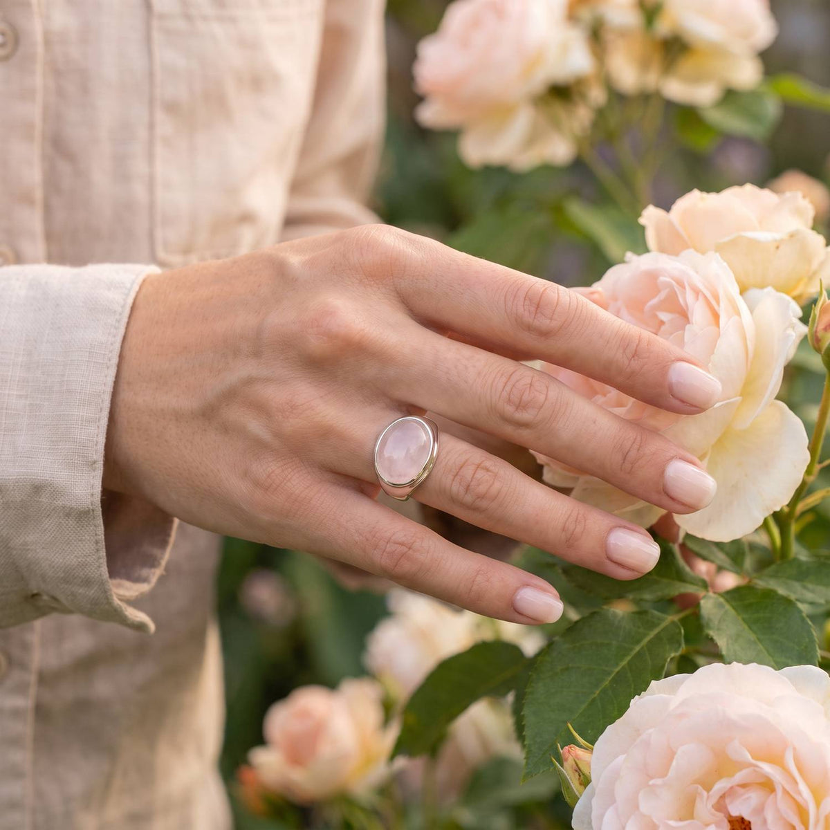 Silberring mit Rosenquarz an der Hand zwischen Blumen