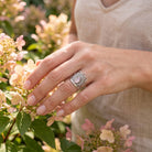 [KI] Silberring mit Rosenquarz an der Hand zwischen Blumen