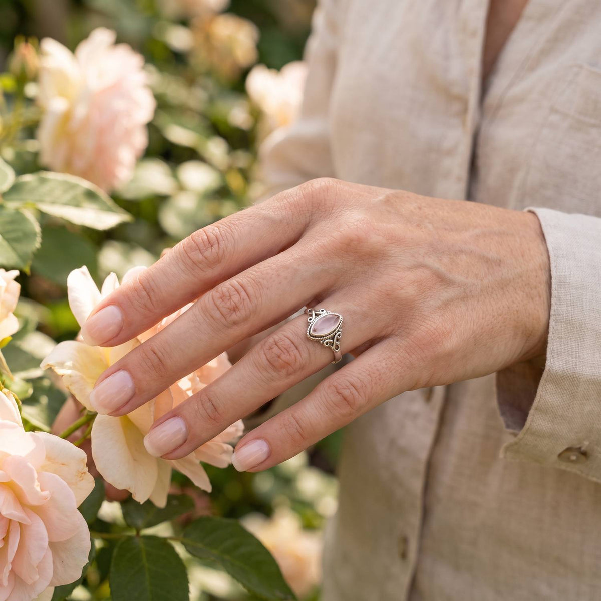 Silberring mit Rosenquarz an der Hand zwischen Blumen