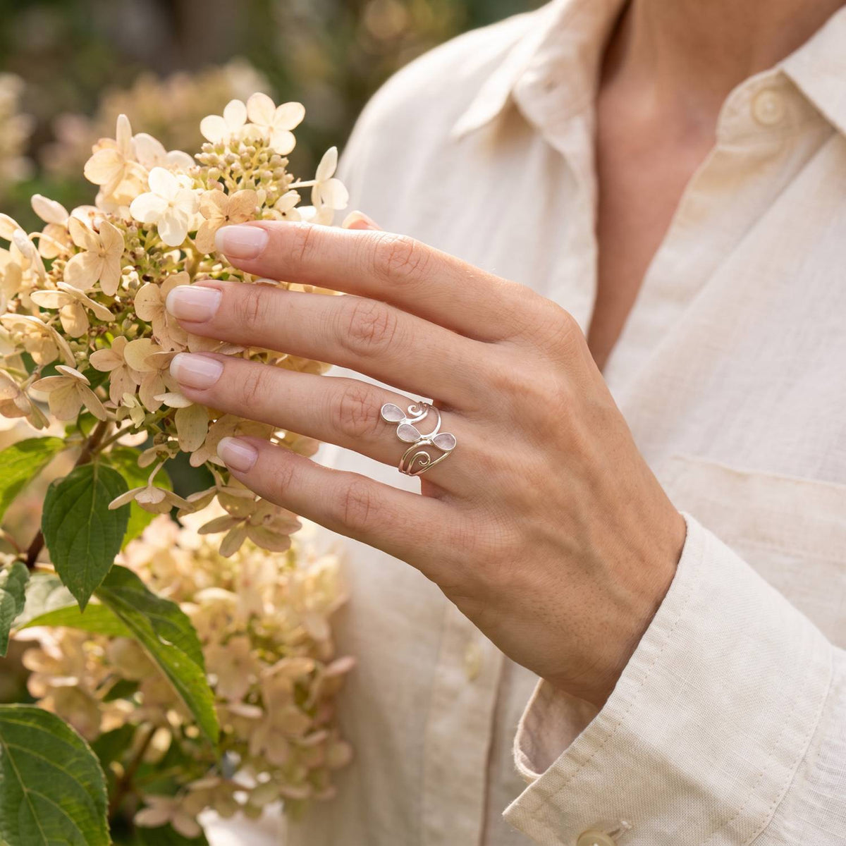 Silberring mit Rosenquarz an der Hand zwischen Blumen