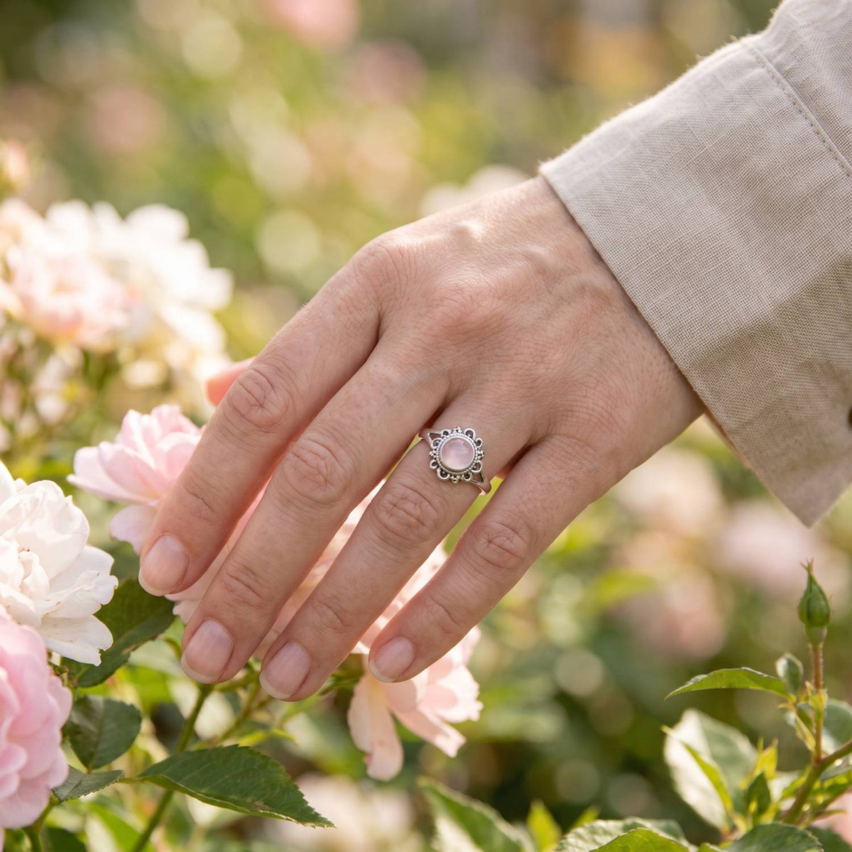 Silberring mit Rosenquarz an der Hand zwischen Blumen