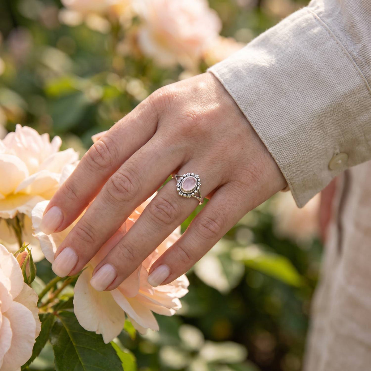 Silberring mit Rosenquarz an der Hand zwischen Blumen
