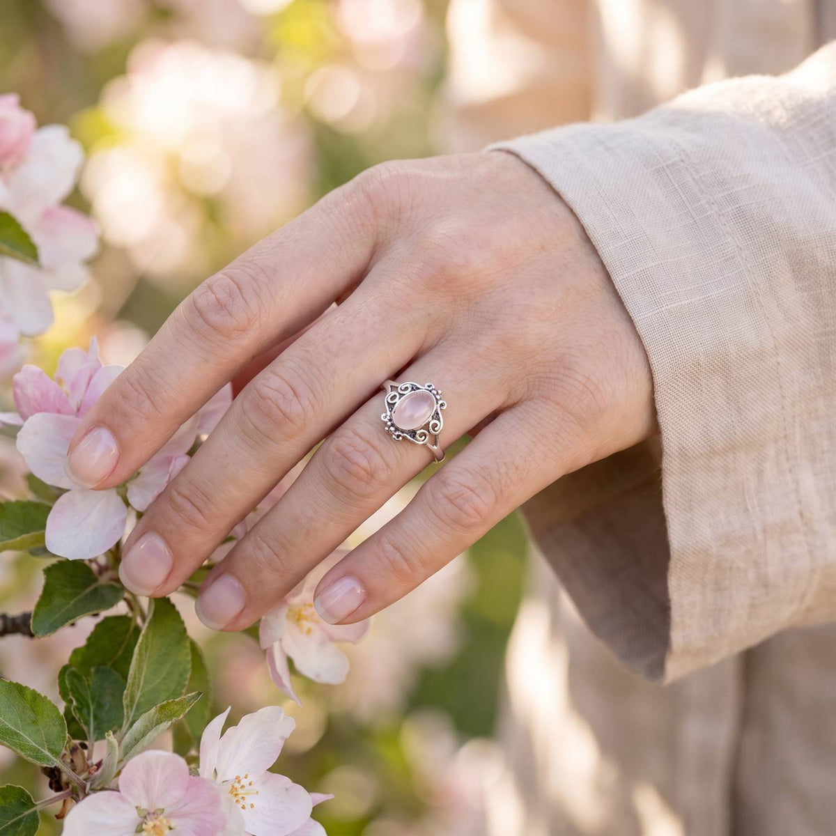 Silberring mit Rosenquarz an der Hand zwischen Blumen