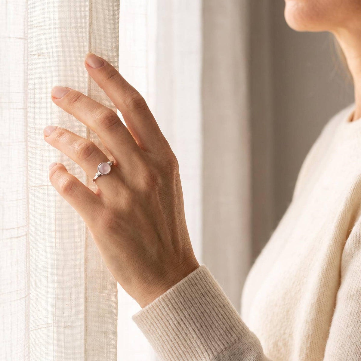 Frau trägt einen Rosenquarzring aus Silber am Fenster